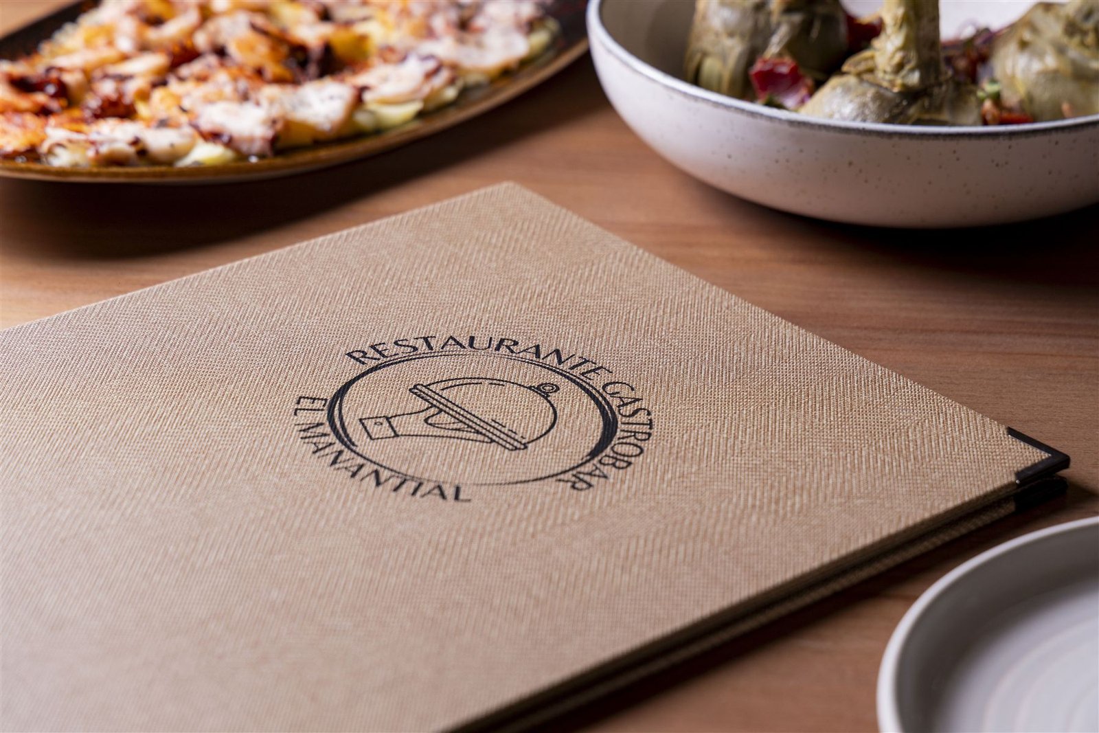 Carta física de El Manantial con el emblema del restaurante sobre la mesa
